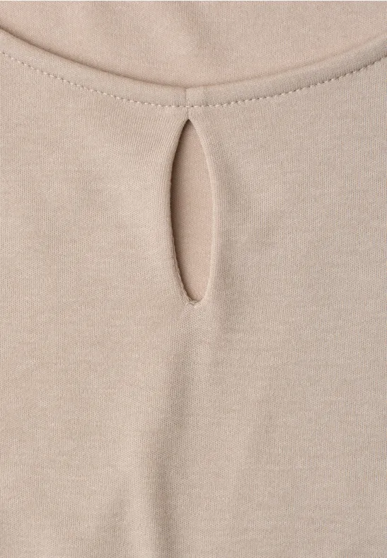 Close-up van een beige top van zacht materiaal met een kleine druppelvormige uitsnijding bij de hals.