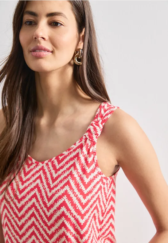 Vrouw met mouwloos topje in roze-wit zigzagmotief, zijwaarts gefotografeerd.