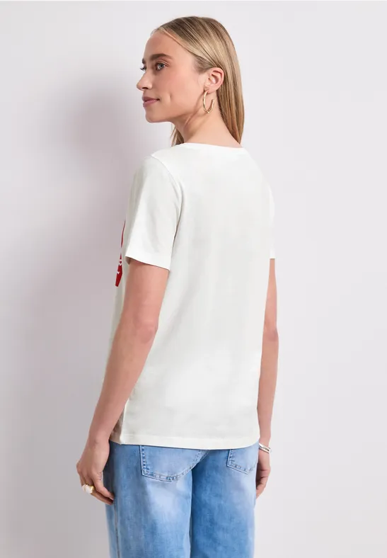 Frau von hinten in weißem T-Shirt und blauer Jeans vor weißem Hintergrund.