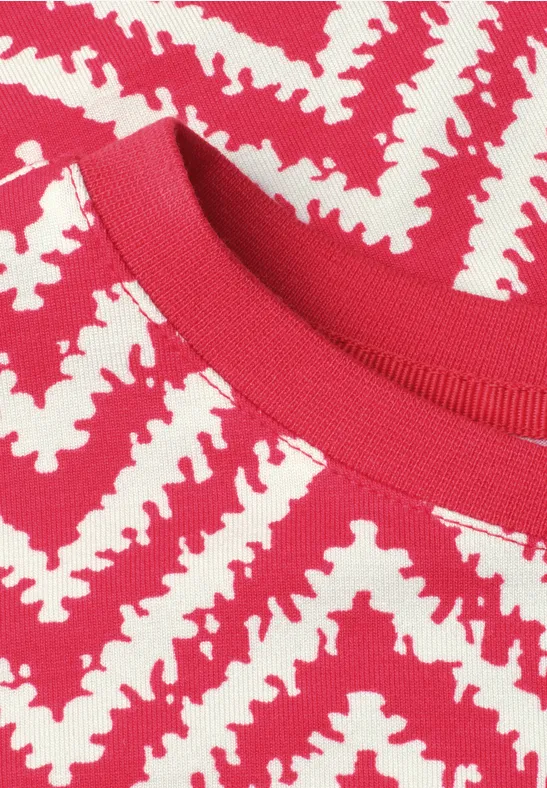Close-up van een rood gebreid shirt met wit zigzagpatroon.