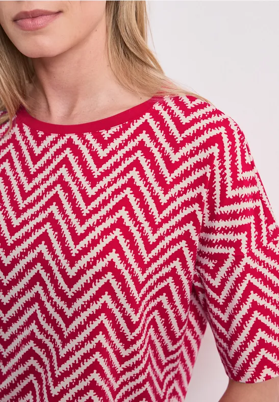 Vrouw draagt rood t-shirt met wit zigzagpatroon, halflange mouwen en ronde hals.