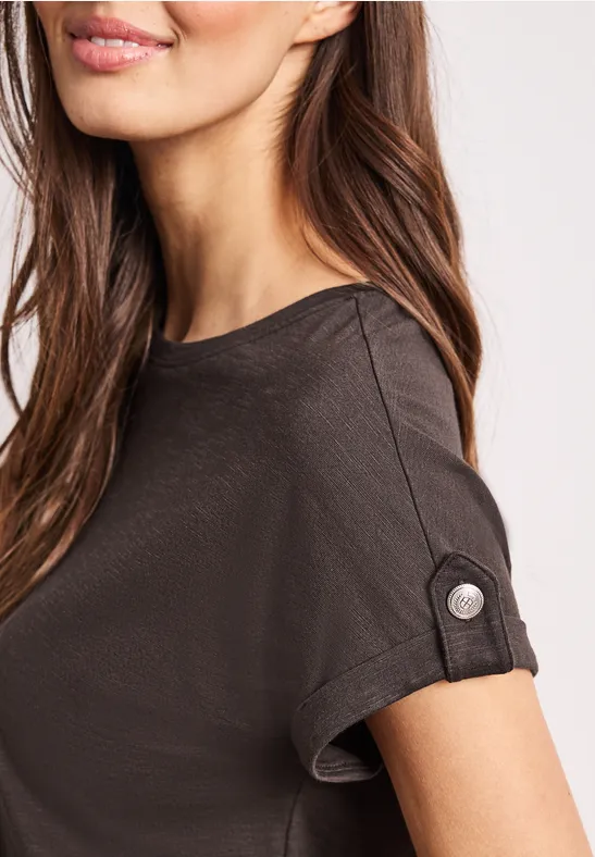 Nahaufnahme einer Frau in einem dunkelgrauen T-Shirt mit gekrempeltem Ärmel und Knopf.