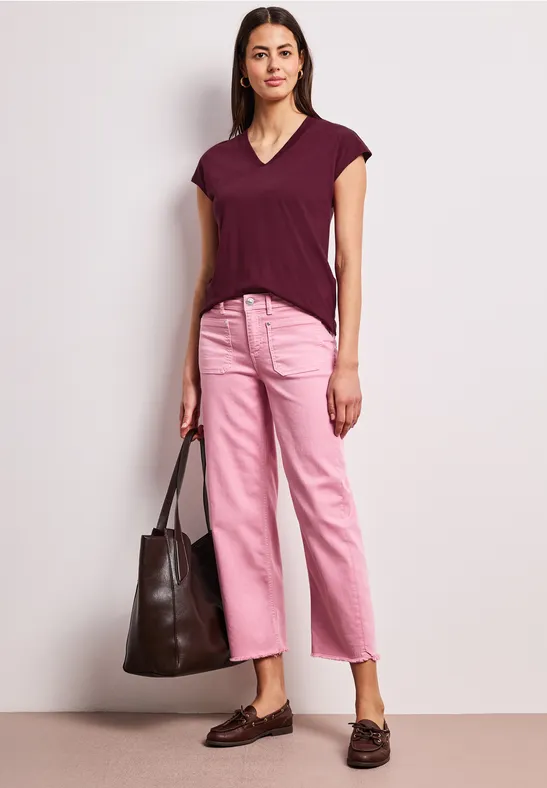 Frau trägt burgunderfarbenes T-Shirt, rosafarbene Culotte-Hose, dunkle Loafer und trägt eine große Tasche.