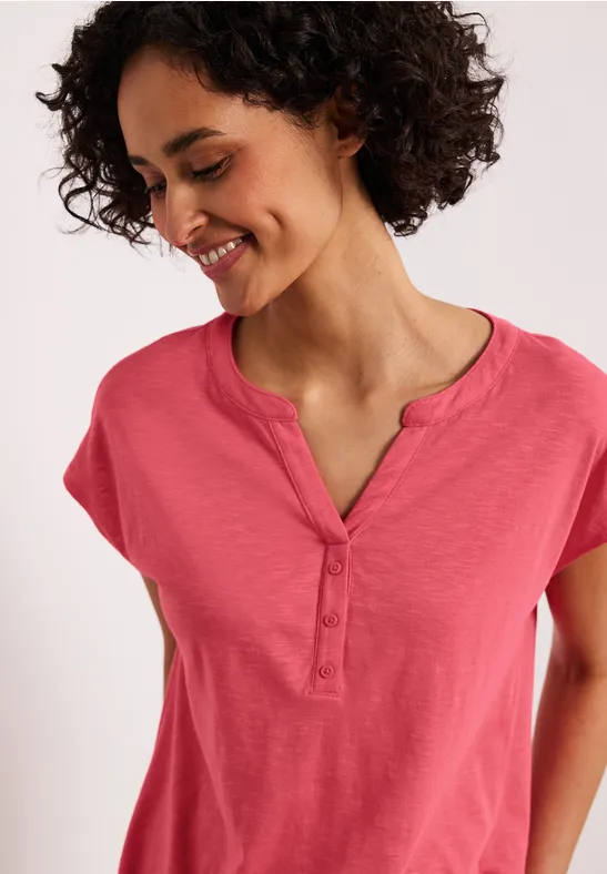 Frau trägt ein rosa Kurzarmshirt mit Knopfleiste, Gesicht unscharf.