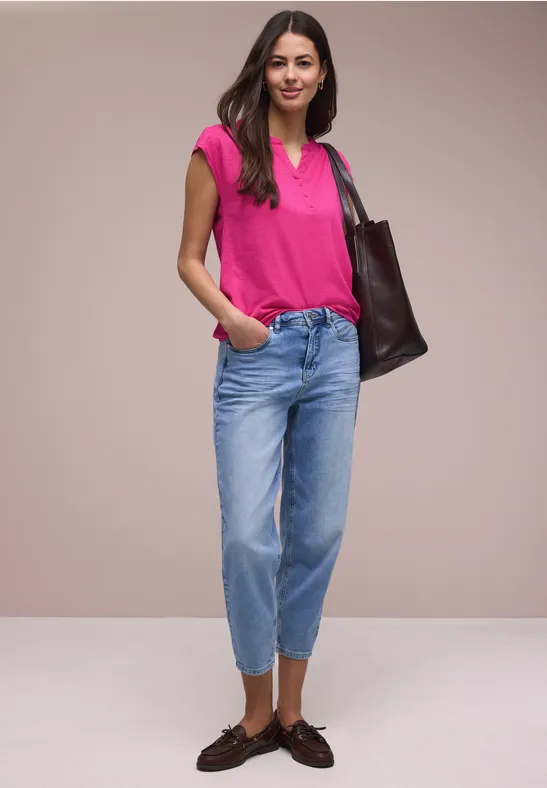 Frau in pinkem T-Shirt, hellblauen, hochgeschnittenen Cropped-Jeans, braunen Loafers und Schultertasche.