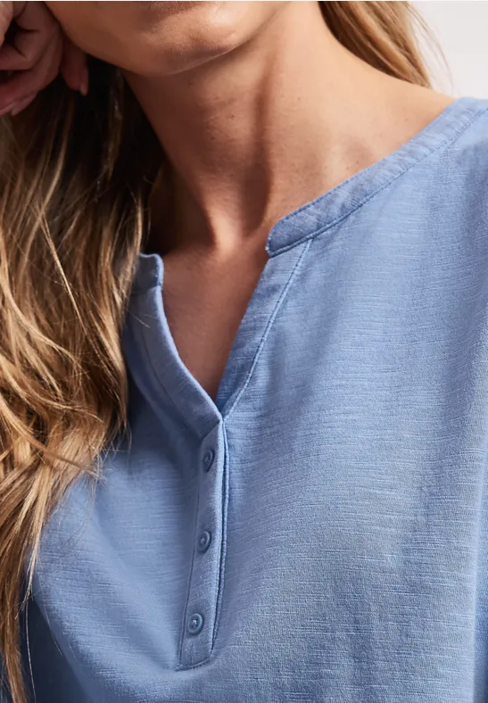 Hals- und Schulterbereich einer Frau in einer hellblauen, geknöpften Bluse