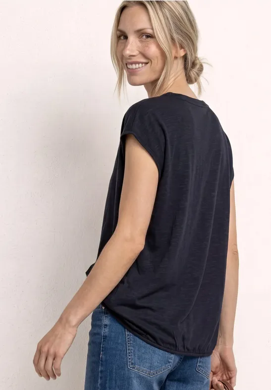 Frau von hinten in schwarzem T-Shirt und Jeans vor hellem Hintergrund.