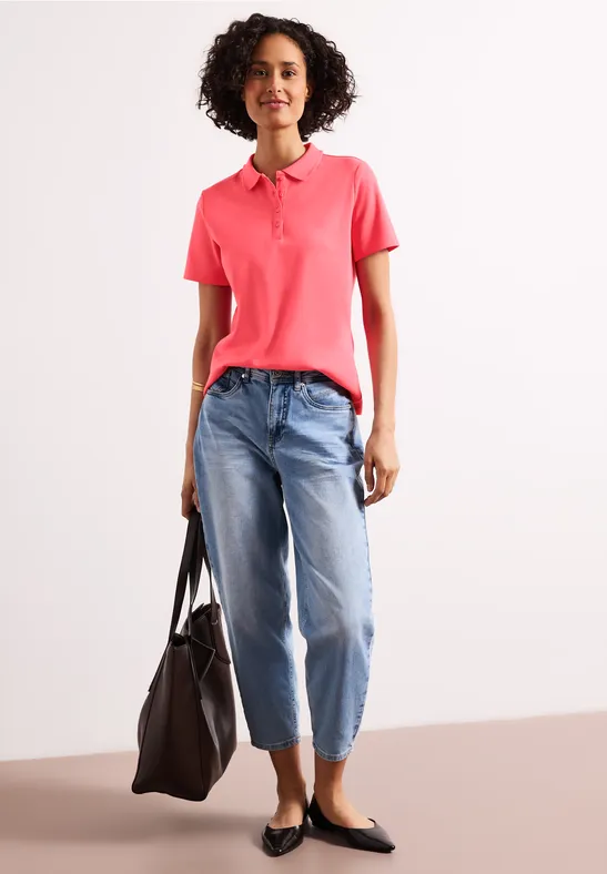 Frau in pinkem Poloshirt, Jeans, schwarzen Ballerinas und großer schwarzer Tasche.