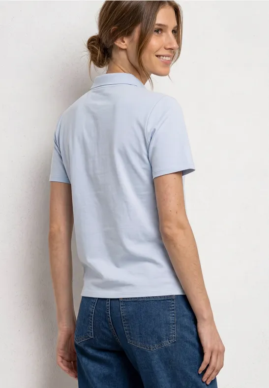Frau von hinten in hellblauem Poloshirt und Jeans mit Dutt.
