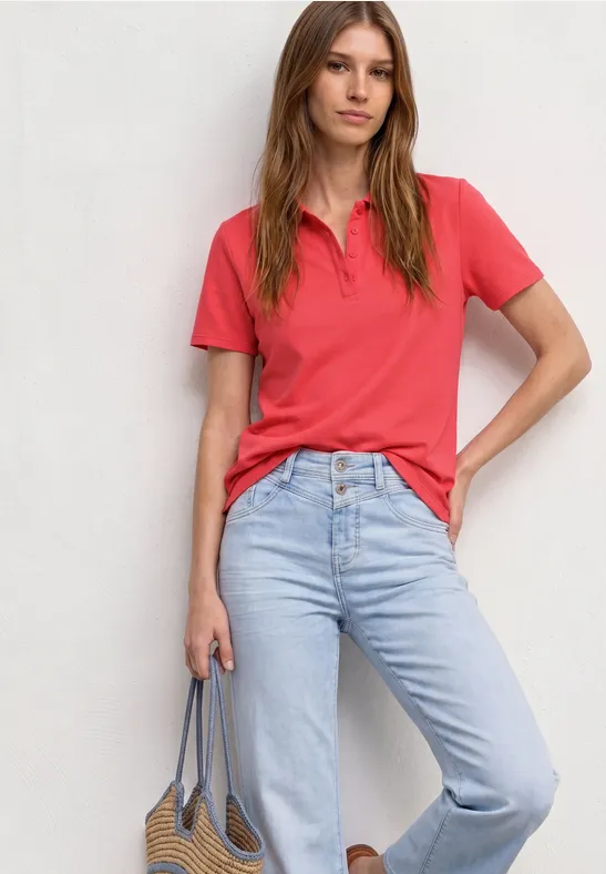 Een persoon draagt een rood T-shirt, een lichtblauwe spijkerbroek en houdt een tas voor een witte achtergrond.