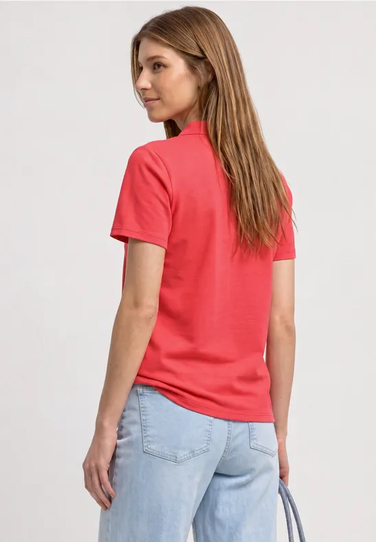 Vrouw van achteren in een rood T-shirt en lichte spijkerbroek, met een handtas.