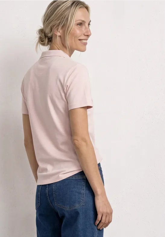Femme de dos en t-shirt rose et jean bleu devant un fond clair et épuré.