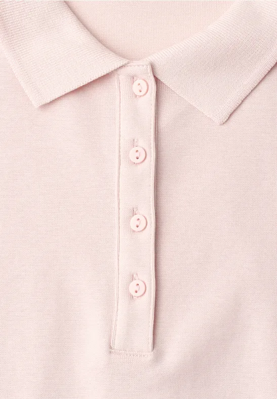 Gros plan d’un polo rose pastel avec col et quatre boutons.