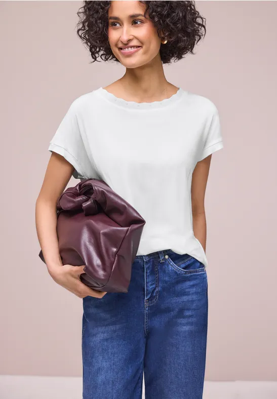 Person in weißem T-Shirt und Jeans hält eine große violette Clutchbag unter dem Arm.