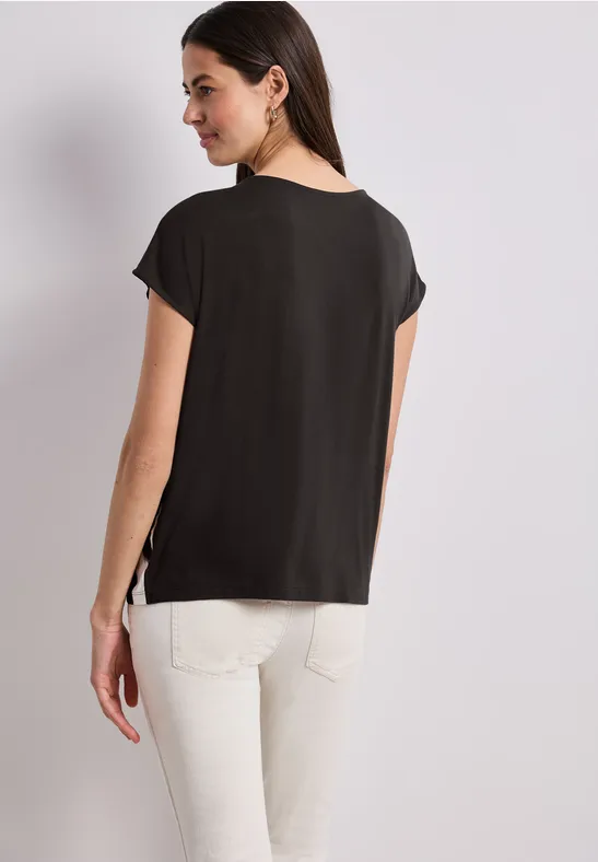 Frau von hinten, schwarze Kurzarmbluse, weiße Hose.