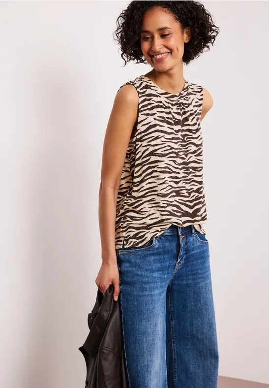 Vrouw draagt een zebraprint top, wijde jeans en houdt een zwarte tas vast.