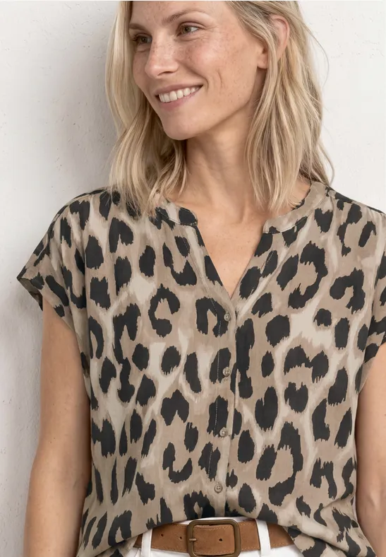 Lachende vrouw in beige luipaardprintblouse met korte mouwen en een bruine riem.