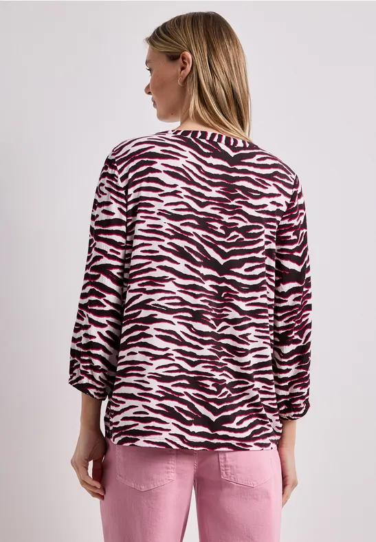 Frau von hinten in rosa-schwarzem Zebra-Print-Oberteil und rosa Hose.