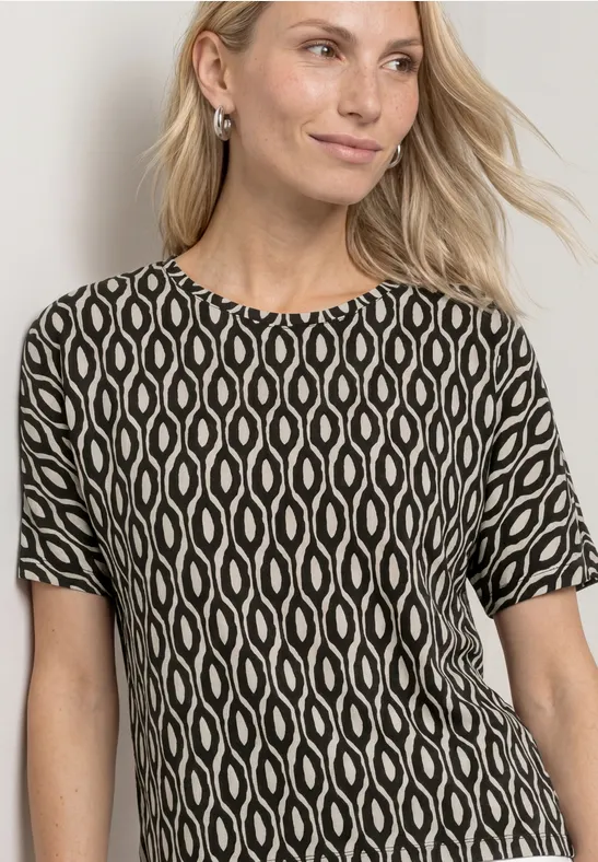 Blonde vrouw in zwart-wit T-shirt met organisch patroon, frontaal gefotografeerd voor lichte achtergrond.