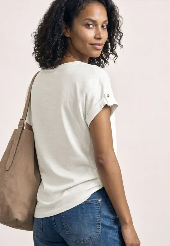 Rückansicht einer Frau mit lockigem Haar, weißem T-Shirt, Jeans und großer hellbrauner Tasche.