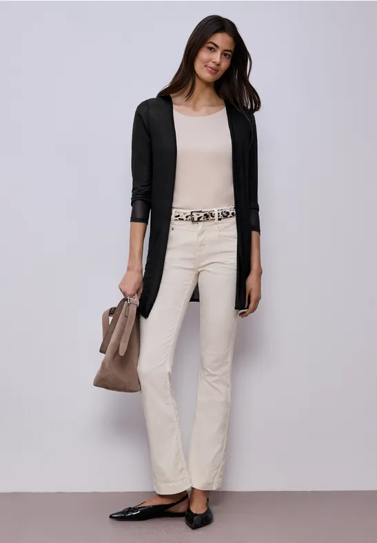 Frau mit schwarzem Cardigan, hellem Top, weißen Hosen, schwarzen Ballerinas und brauner Handtasche.
