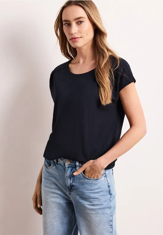 Vrouw in zwart T-shirt en lichtblauwe jeans tegen neutrale achtergrond.