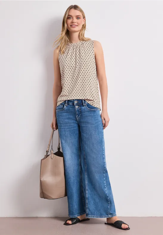 Femme en top sans manches beige, jean large, sandales noires et sac beige.