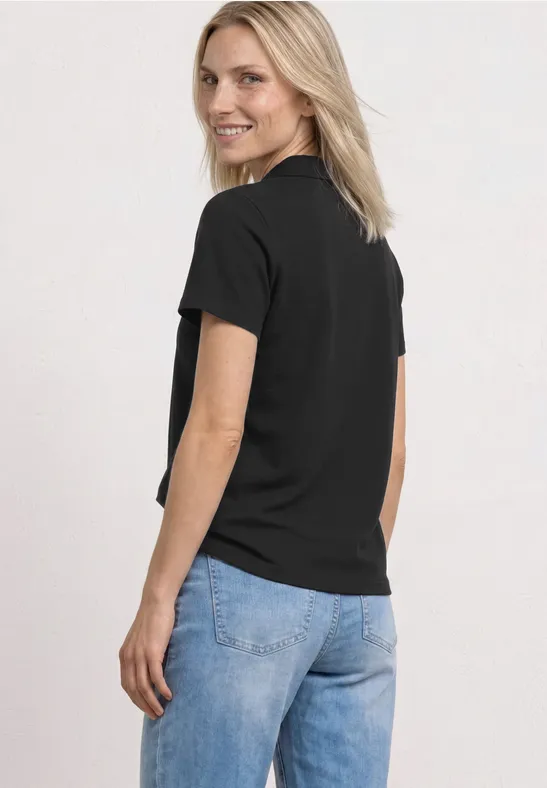 Une femme de profil porte un t-shirt noir et un jean bleu sur fond blanc.