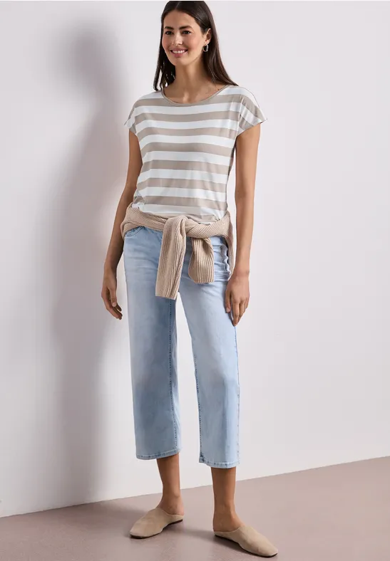 Femme en t-shirt rayé, jean clair, sweat noué à la taille et mocassins beige.