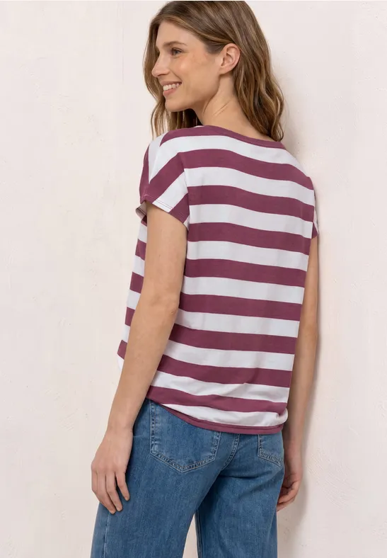 Vrouw van achter gefotografeerd in wit-bordeaux gestreept T-shirt en blauwe jeans.