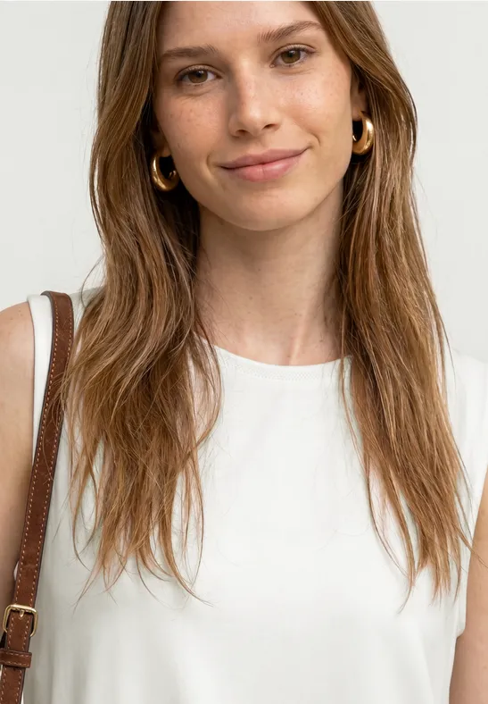 Vrouw met lang bruin haar in een wit mouwloos topje en een bruine schoudertas.