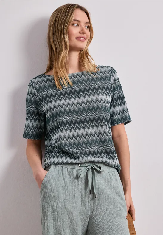 Vrouw met een kortärmelig shirt met zigzagpatroon en een losse, lichtgroene broek.