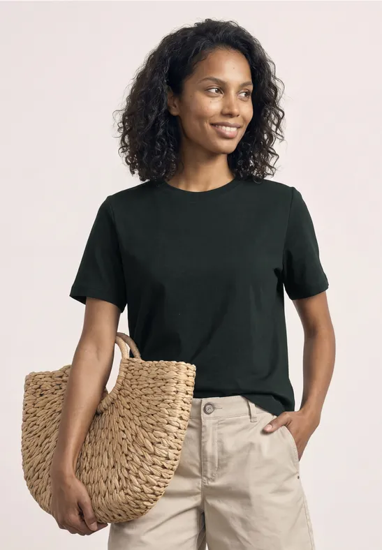 Frau in schwarzem T-Shirt und beiger Hose hält eine große geflochtene Strohtasche.