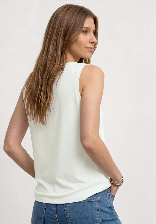 Femme de dos portant un débardeur blanc, main dans la poche arrière, cheveux bruns mi-longs.