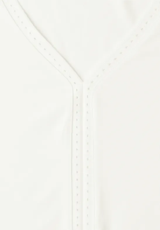 Vêtement blanc à encolure en V orné de fines broderies ajourées.