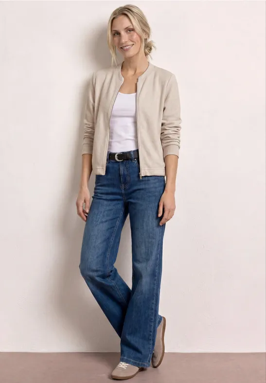 Femme en t-shirt blanc, veste beige, jean large et mocassins sur fond clair.