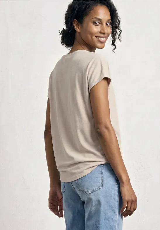 Rückansicht einer Person in beige T-Shirt und Jeans vor hellem Hintergrund.