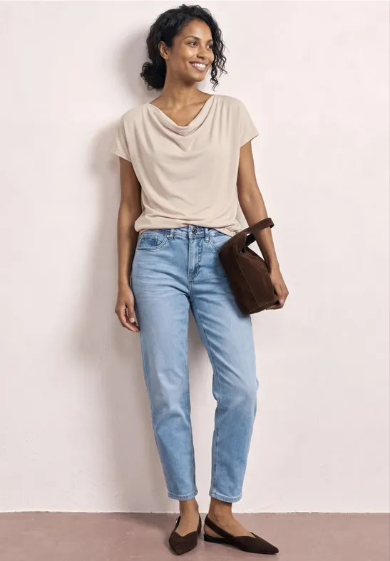 Frau in weißem Top, blauen Jeans, brauner Umhängetasche und braunen Ballerinas.