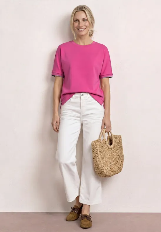 Vrouw in roze T-shirt en witte broek met strooien tas