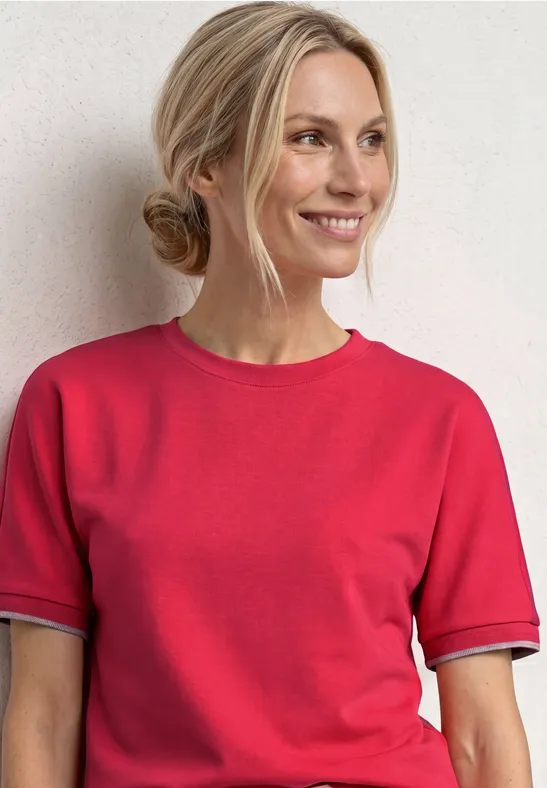 Vrouw met opgestoken haar draagt rood t-shirt voor een lichte achtergrond.