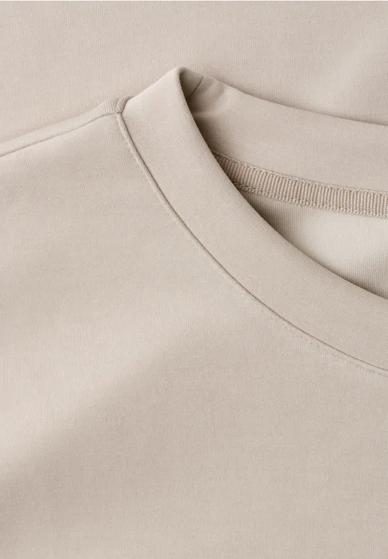 Close-up van een beige T-shirt met ronde hals en nette naden