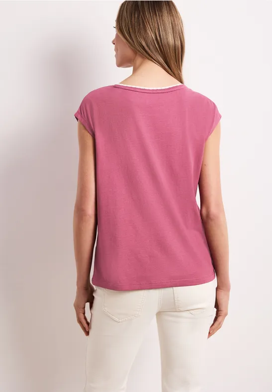 Vrouw van achteren in een roze T-shirt en lichte broek tegen neutrale achtergrond.