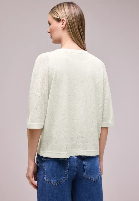 Frau von hinten in cremefarbenem Pullover mit halblangen Ärmeln und blauen Jeans.