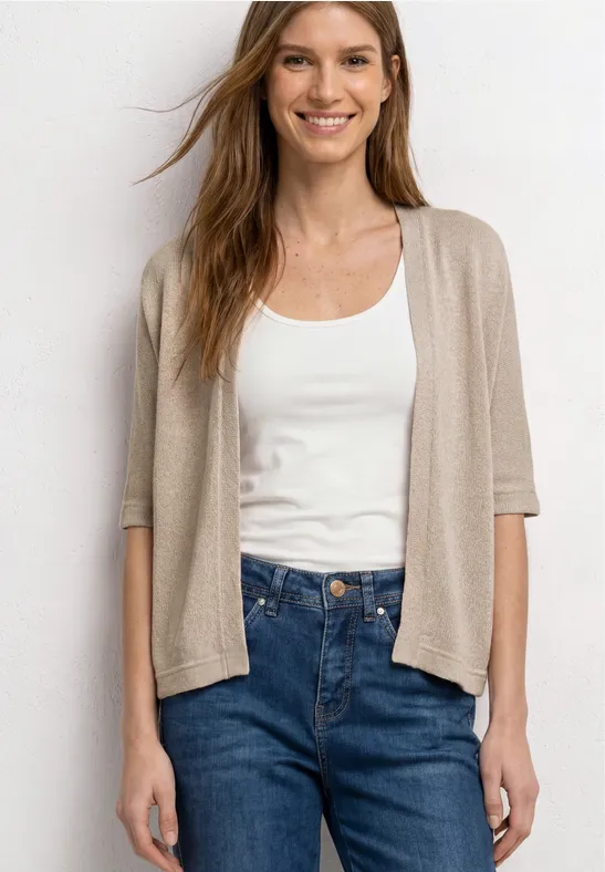 Vrouw met een witte tanktop, beige kortarmvest en blauwe high-waist jeans.