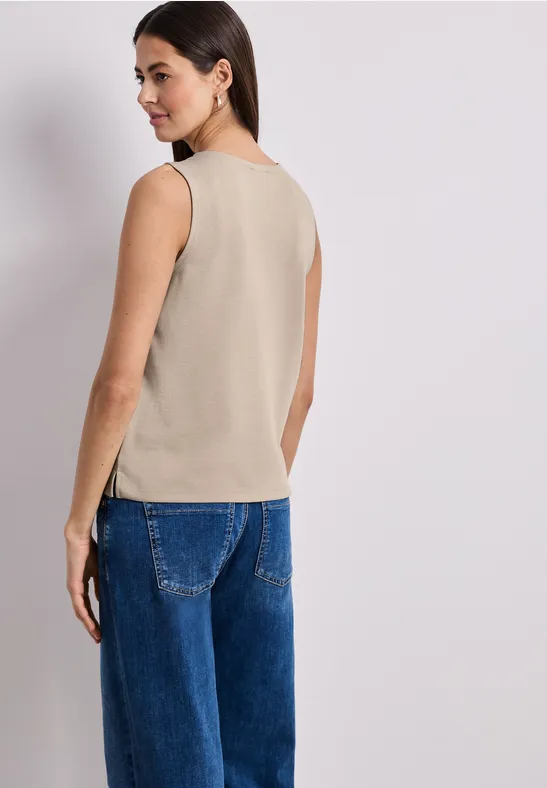 Femme de dos, portant un haut sans manches beige et un jean bleu ample.