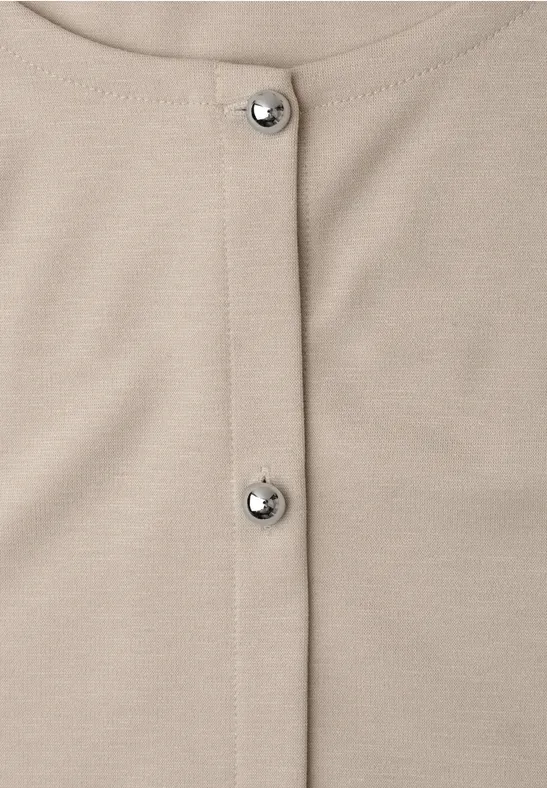 Gros plan d’un vêtement beige avec deux boutons-pression argentés au centre.