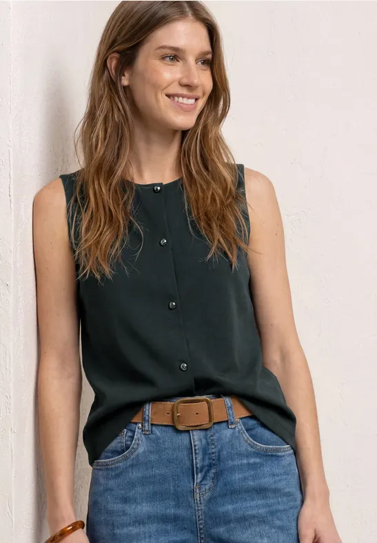 Une femme aux cheveux lâchés porte un top noir sans manches, un jean bleu et une ceinture marron.