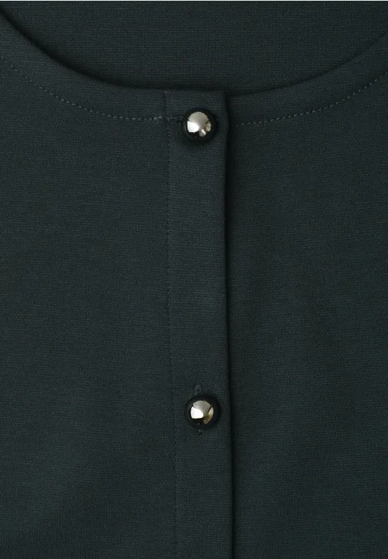 Gros plan sur un haut vert foncé avec deux boutons nacrés brillants