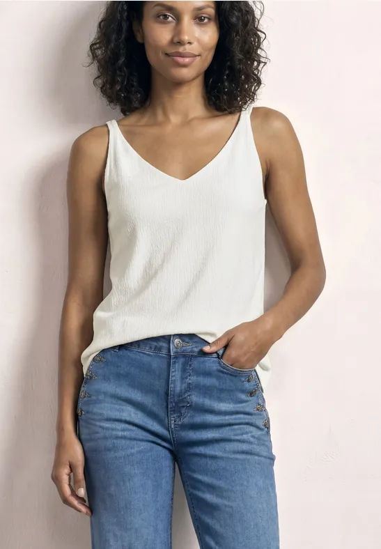 Femme aux cheveux bouclés porte un haut blanc et un jean bleu, posant de manière détendue.