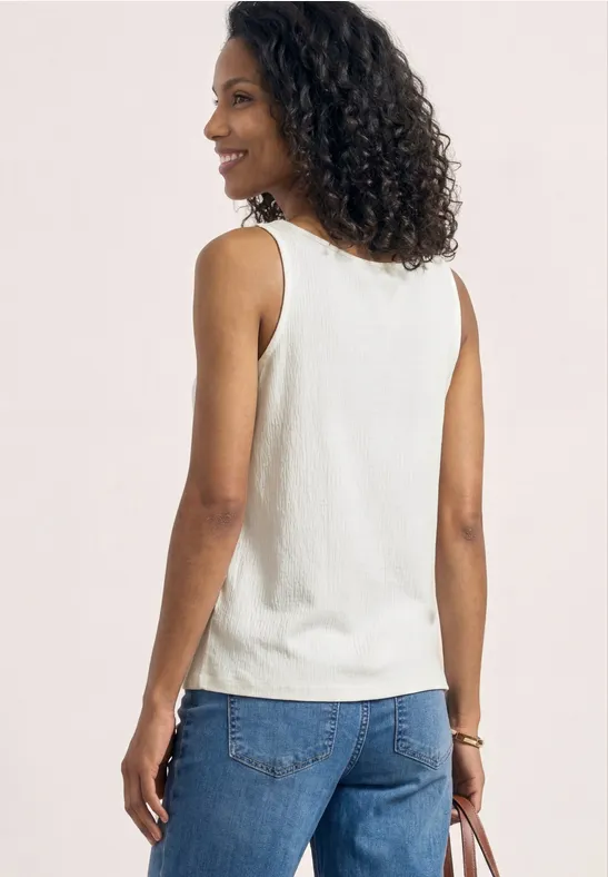 Personne de dos aux cheveux bouclés, vêtue d'un débardeur blanc et d'un jean bleu sur fond neutre.